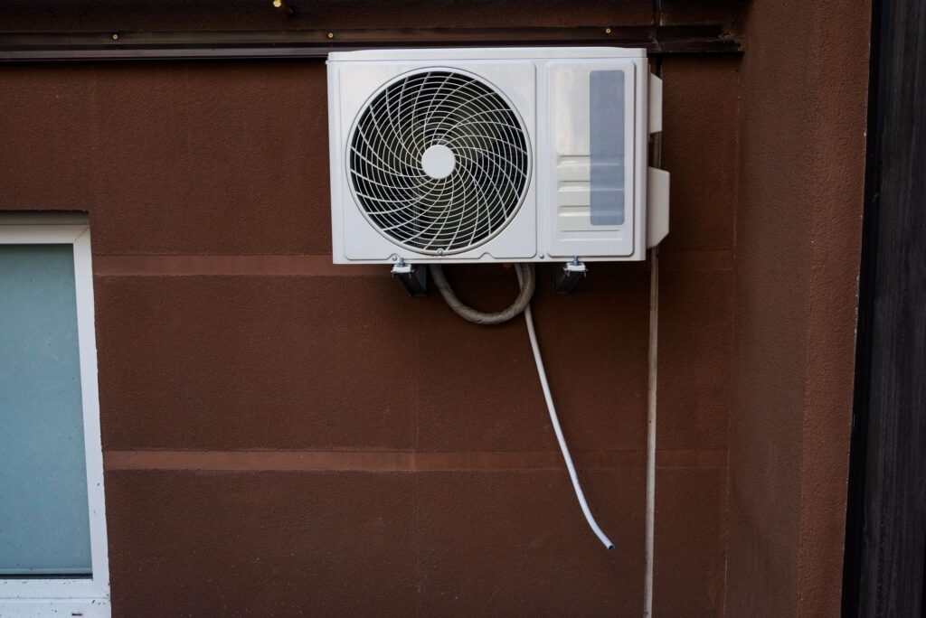 Outdoor air conditioning unit mounted on the exterior wall of a residential building. Medium shot